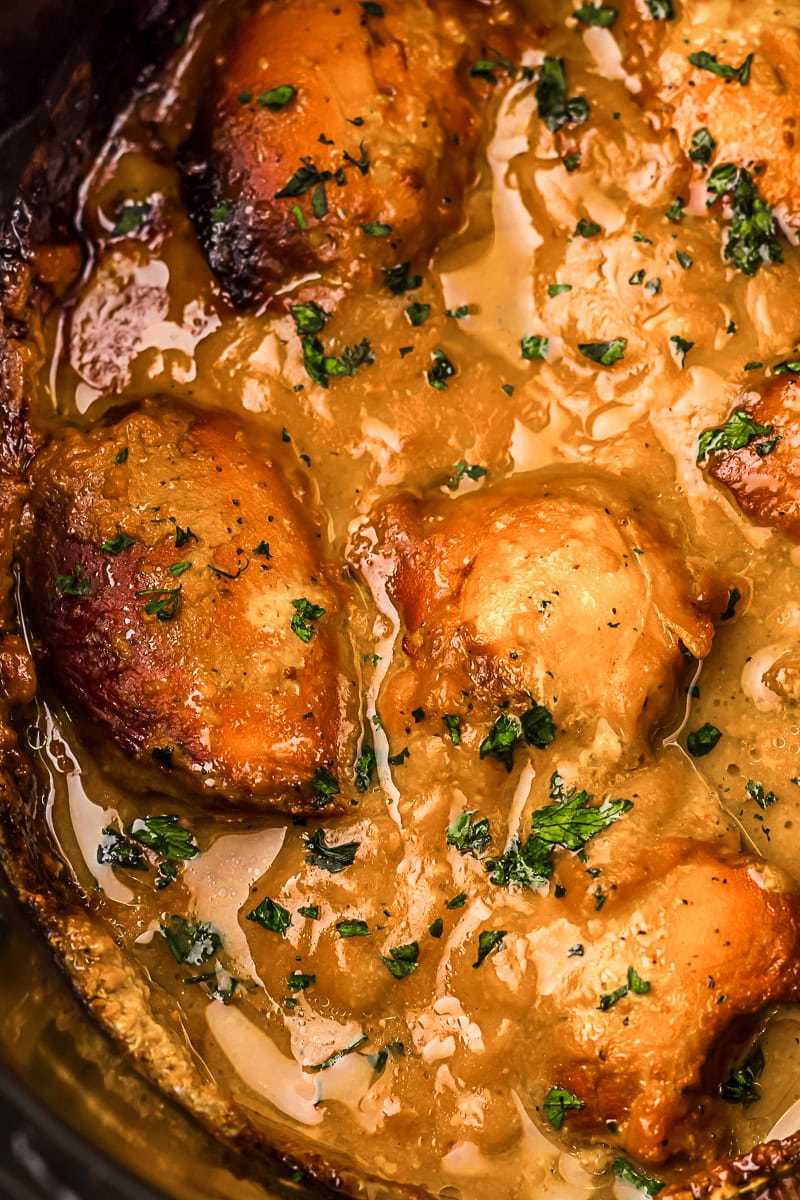 Golden brown chicken thighs simmering in a creamy sauce, garnished with chopped herbs in a pan.