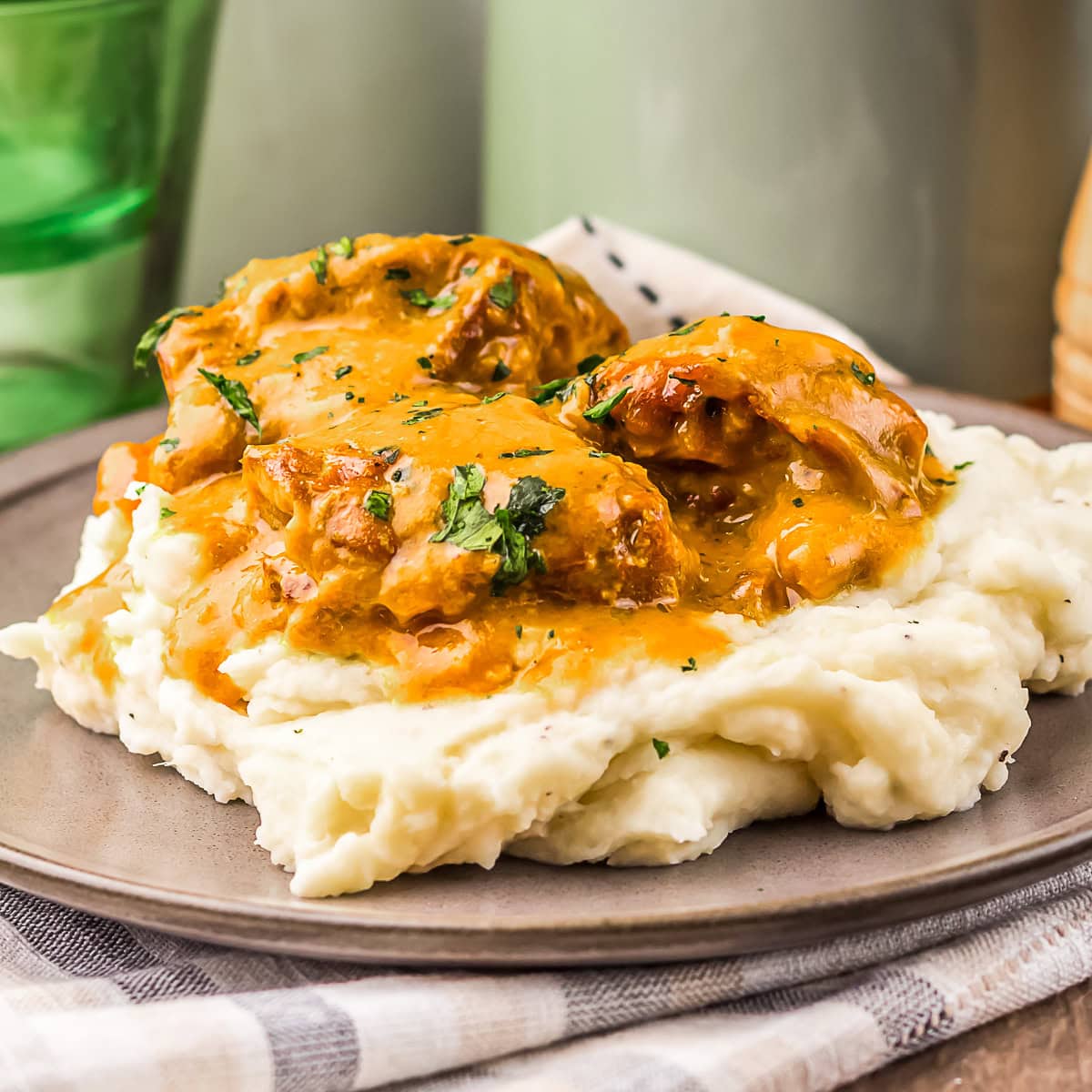 Mashed potatoes topped with pieces of meat in brown gravy, garnished with chopped herbs, served on a gray plate.