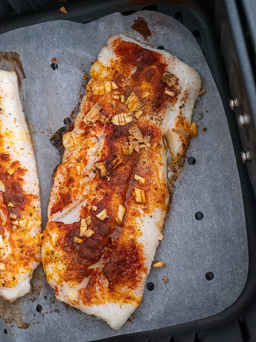 Seasoned fish fillet topped with spices and chopped garlic on parchment paper inside an air fryer basket.