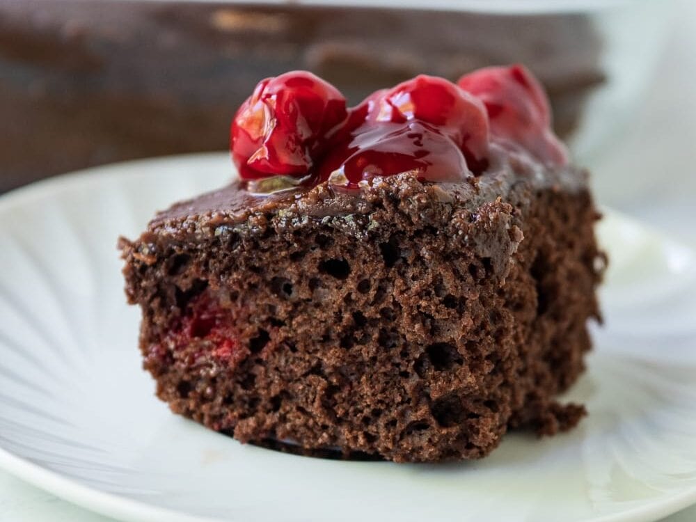 slice of chocolate cherry cake on a plate with cherries on top