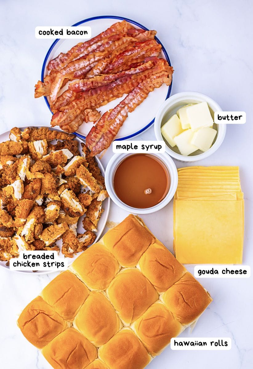 Top-down view of cooked bacon, breaded chicken strips, butter, maple syrup, gouda cheese slices, and Hawaiian rolls arranged on a white surface, each labeled with text.