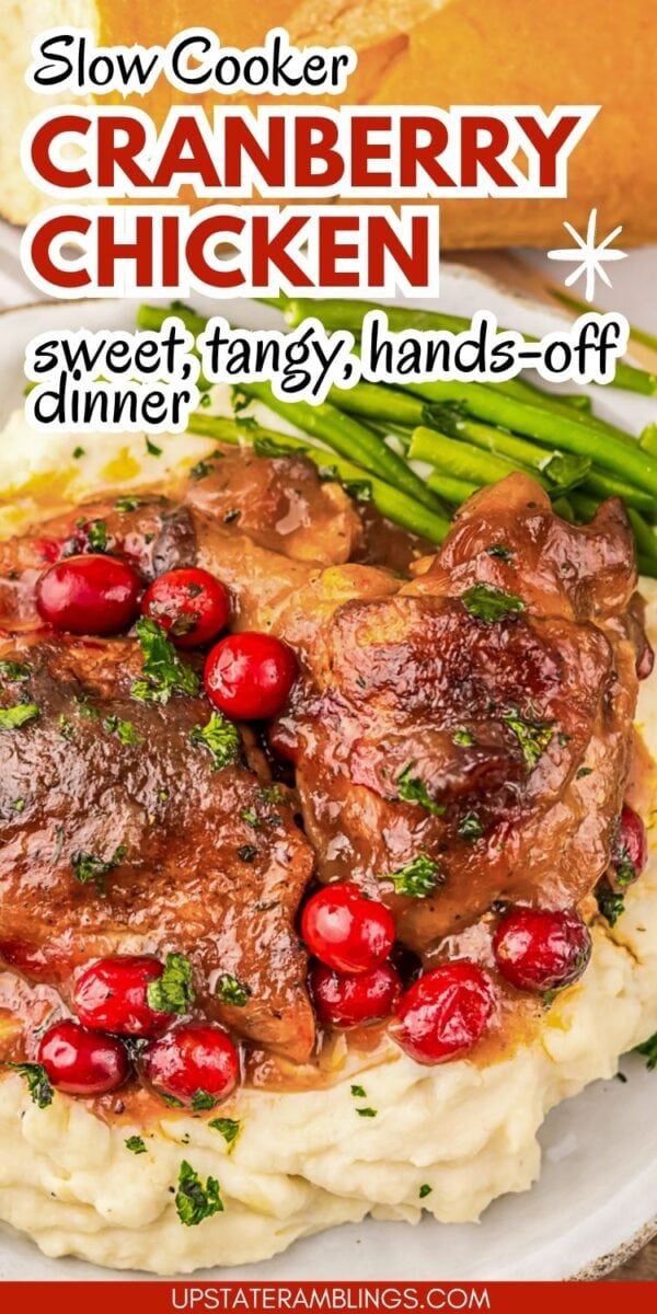 Slow-cooked cranberry chicken served over mashed potatoes, garnished with cranberries and herbs, with green beans and bread in the background.