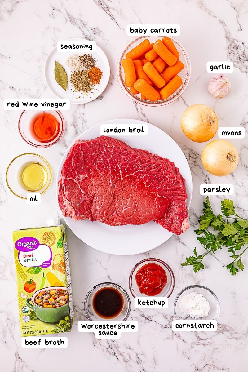 Raw London broil steak surrounded by labeled ingredients including vegetables, seasonings, liquids, cornstarch, ketchup, and beef broth on a marble surface.