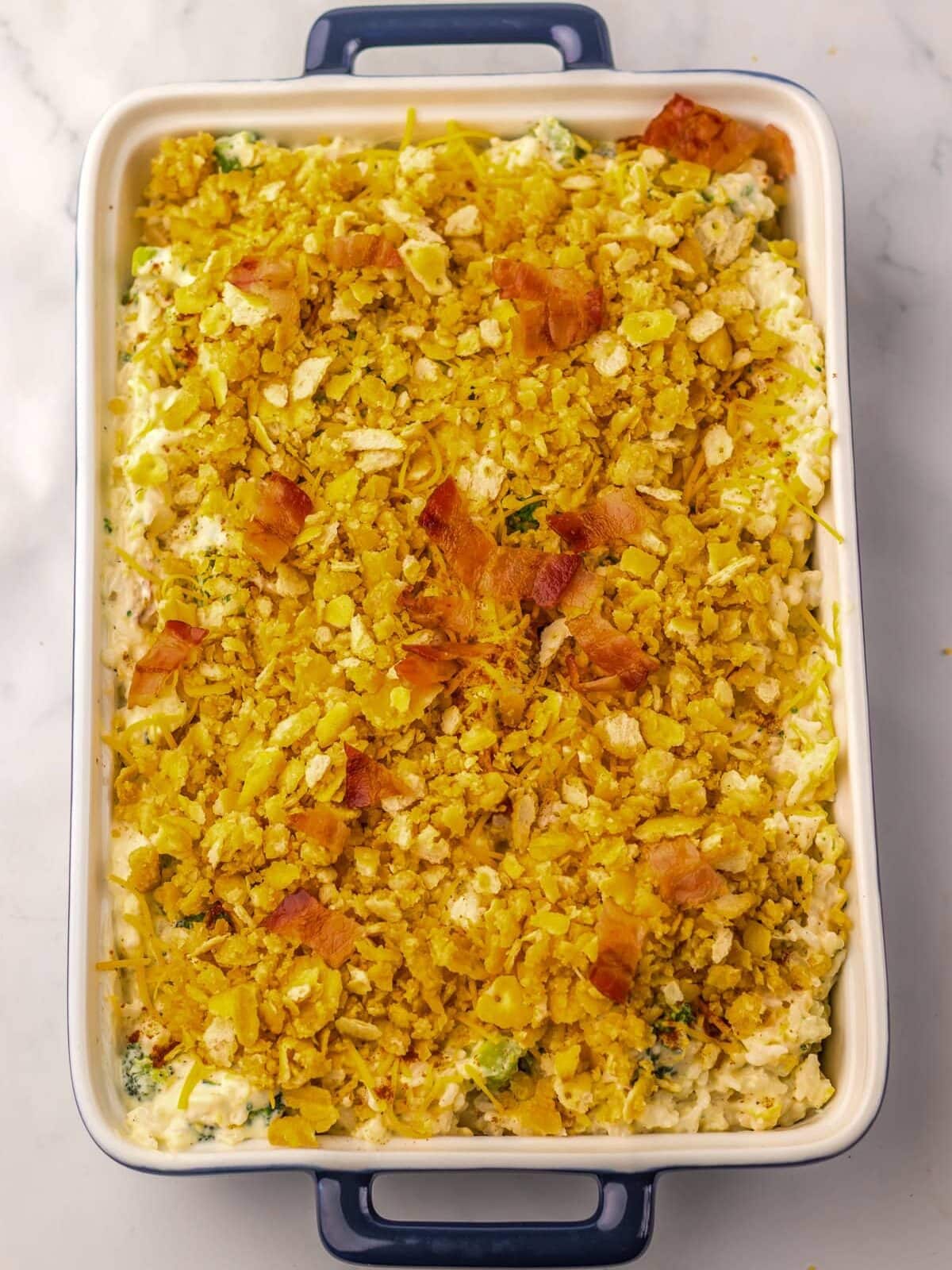 Rectangular casserole dish filled with a creamy mixture topped with a golden, crispy, crumbled topping, resting on a white marble surface.