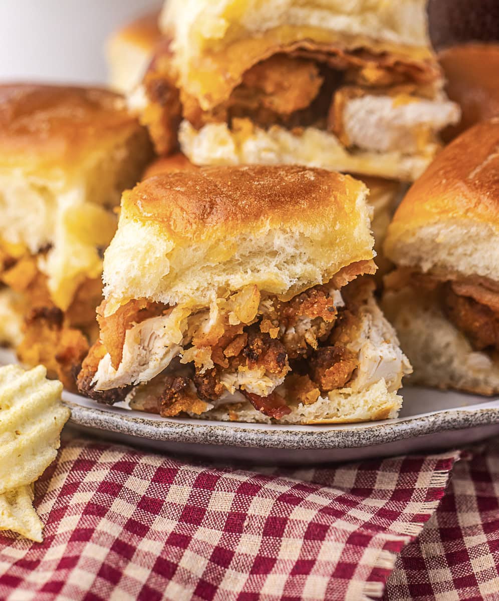 A plate of fried chicken sliders on soft buns, served with potato chips on a checked cloth.