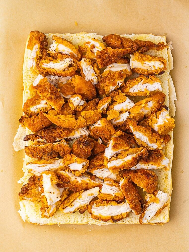 Rectangular piece of bread topped with sliced breaded chicken strips, placed on a sheet of brown parchment paper.