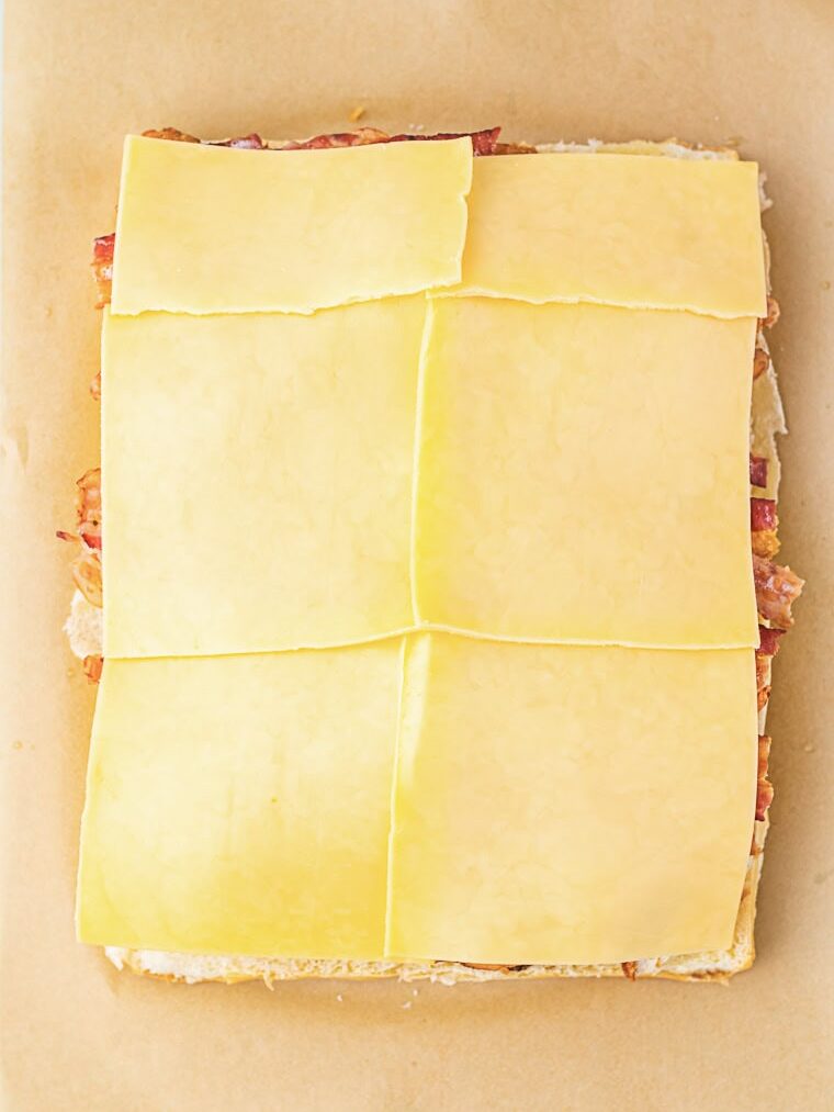 Six slices of cheese are laid out in a rectangular arrangement on top of layered sandwich fillings on parchment paper.
