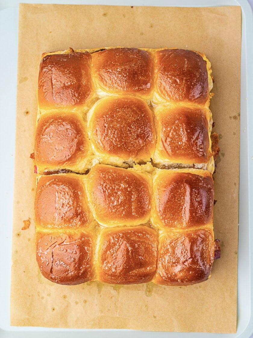A batch of golden brown dinner rolls sits on parchment paper atop a white tray.