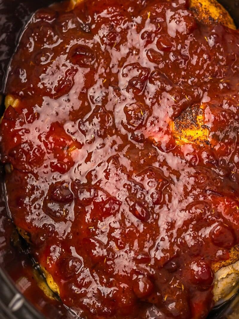 Chicken breasts covered in a thick, red cranberry sauce inside a slow cooker.