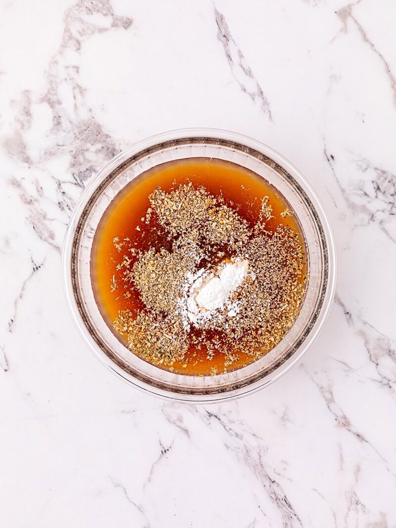 A glass bowl with brown liquid, ground seeds, and white powder sits on a white marble surface.